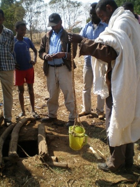 A hydrologist shows citizen scientists how to use simple equipment (a yellow plastic bucket tied to a long length of string) to measuring shallow groundwater levels via a small well, Ethiopia